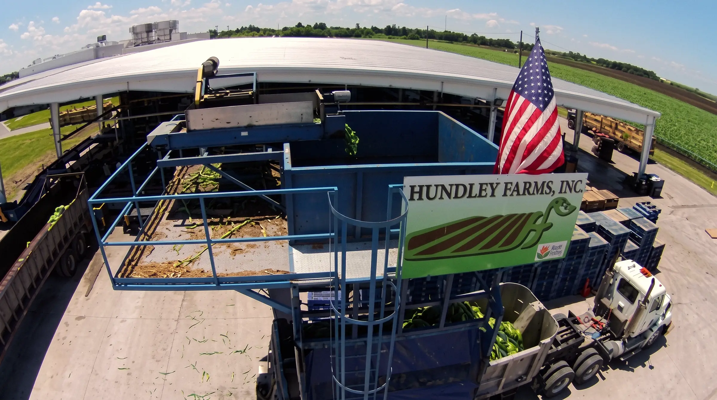 The Hundley Farms packing line under the packing house roof with the farm sign and an American flag