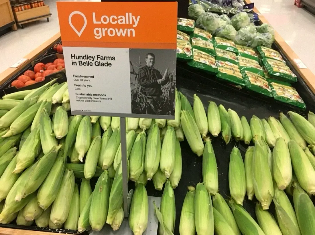 A supermarket produce display of Hundley Farms sweet corn with a Locally Grown sign naming Hundley Farms in Belle Glade